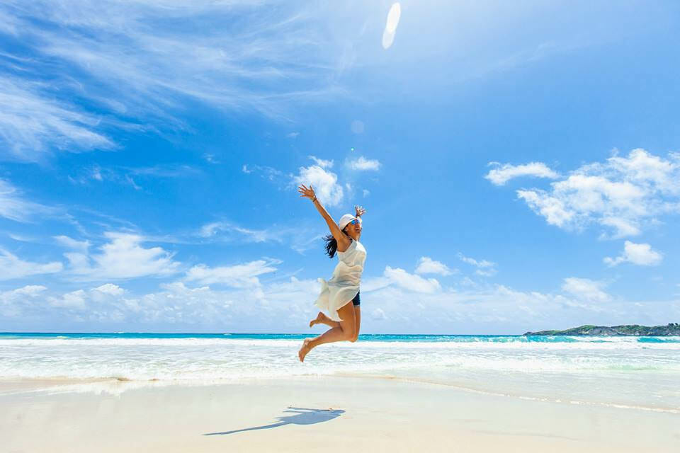 Woman in white coverup and hat jumping on the beach in Punta Cana, Dominican Republic